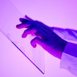 Mãos interagem com uma interface digital transparente iluminada em tons de roxo