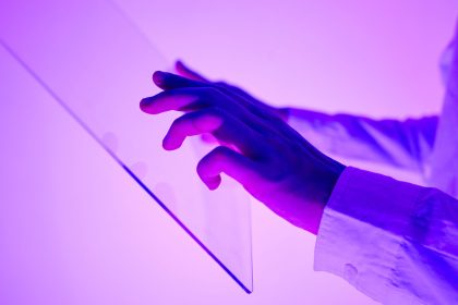 Mãos interagem com uma interface digital transparente iluminada em tons de roxo