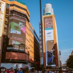Cena urbana movimentada, com grandes painéis digitais de publicidade e edifícios ao redor.
