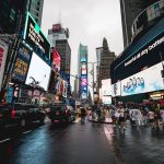 Vista noturna da Times Square, em Nova York, com painéis publicitários iluminados e pessoas circulando.