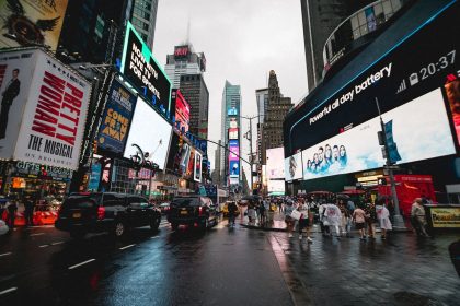 Vista noturna da Times Square, em Nova York, com painéis publicitários iluminados e pessoas circulando.