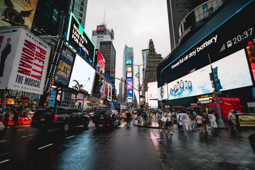 Vista noturna da Times Square, em Nova York, com painéis publicitários iluminados e pessoas circulando.