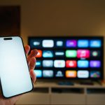 Smart TV exibindo aplicativos em uma sala de estar, com um smartphone em primeiro plano.