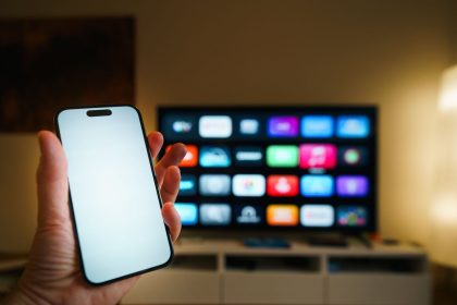 Smart TV exibindo aplicativos em uma sala de estar, com um smartphone em primeiro plano.