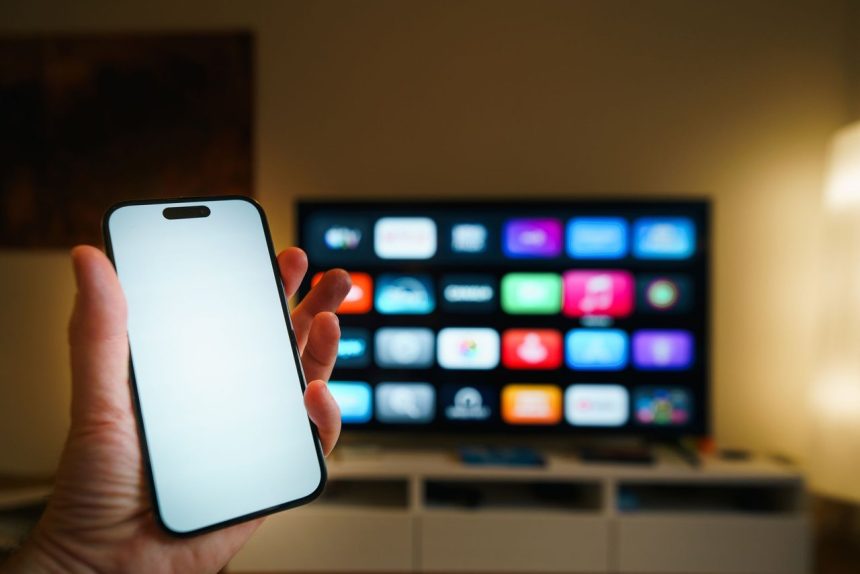 Smart TV exibindo aplicativos em uma sala de estar, com um smartphone em primeiro plano.
